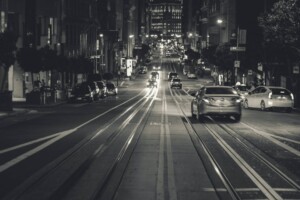 A black and white photo of cars driving down a hill in San Francisco, where car prices and home prices are falling down recently.