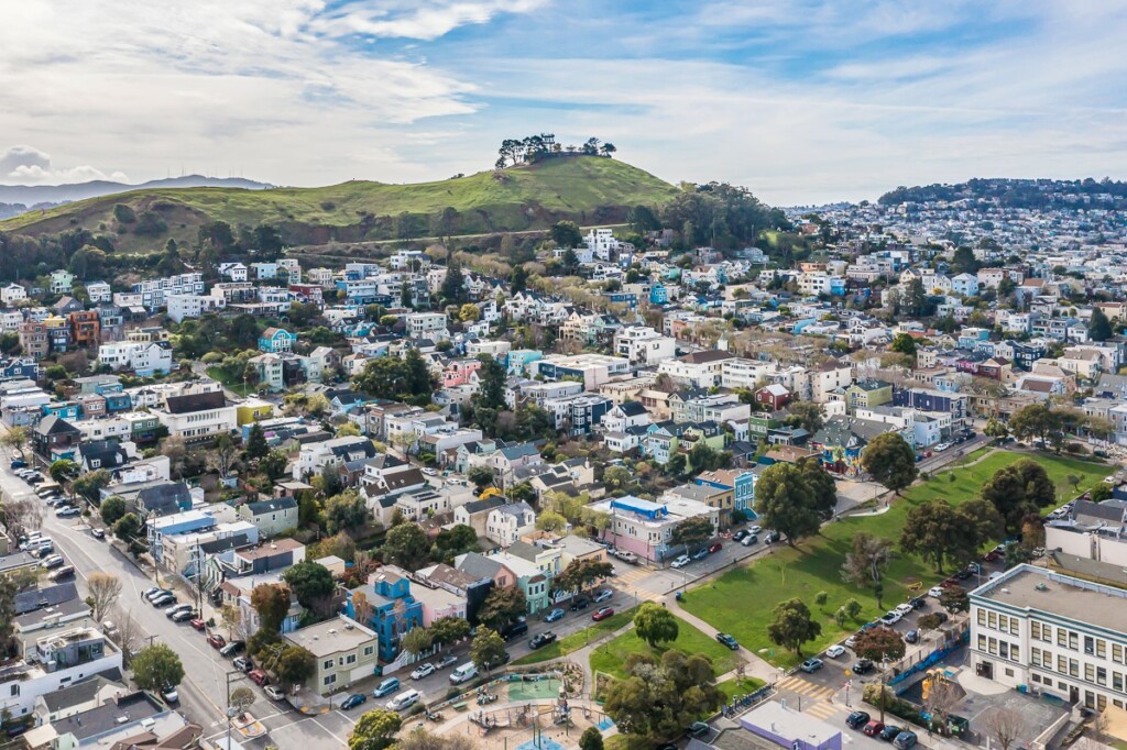 Drone photo from high above Bernal Heights neighborhood homes, showing Bernal Hill in the background.