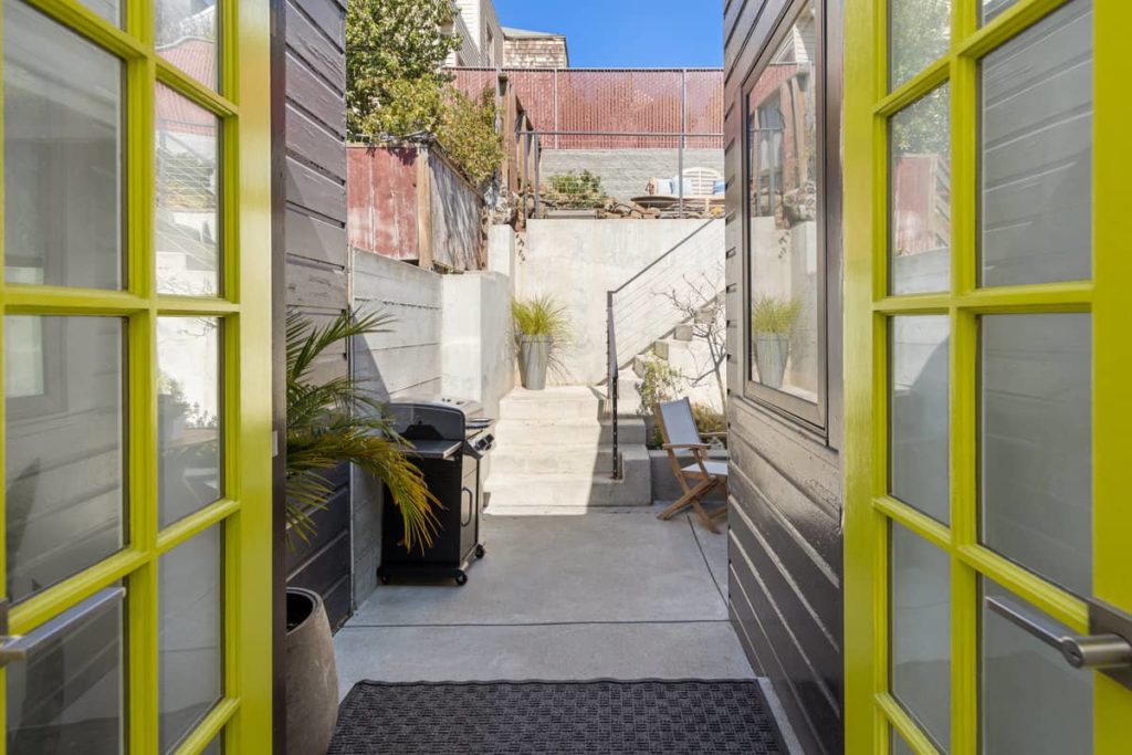 The backyard patio of a home sold in Glen Park, seen through the back doors leading to a concrete patio with stairs and seating.