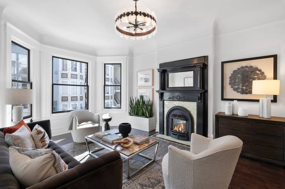 Elegant living room interior in Soma condo featuring an Edwardian fireplace, hardwood floors, and large windows for natural light