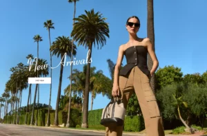 Woman in black top and tan pants standing by palm trees.