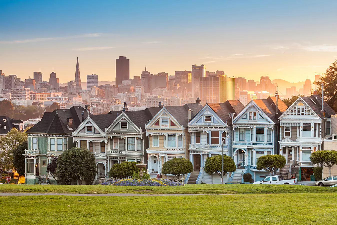 Sunset View of the Painted Lady Victorian-Style homes and the downtown San Francisco skyline from grassy knoll at Alamo Square
