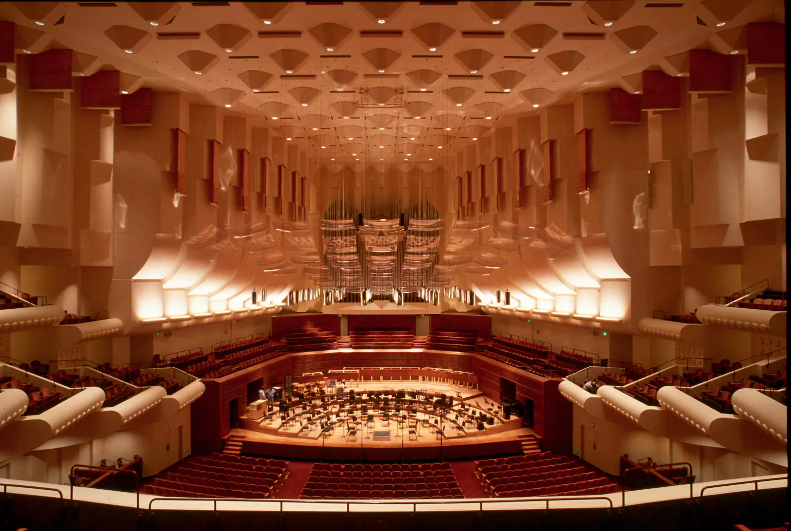 View of the interior of Davies Symphony Hall in San Francisco featuring red seating, warmly lit up interior, ceiling acoustics system, premier balcony box seating, and soaring ceilings