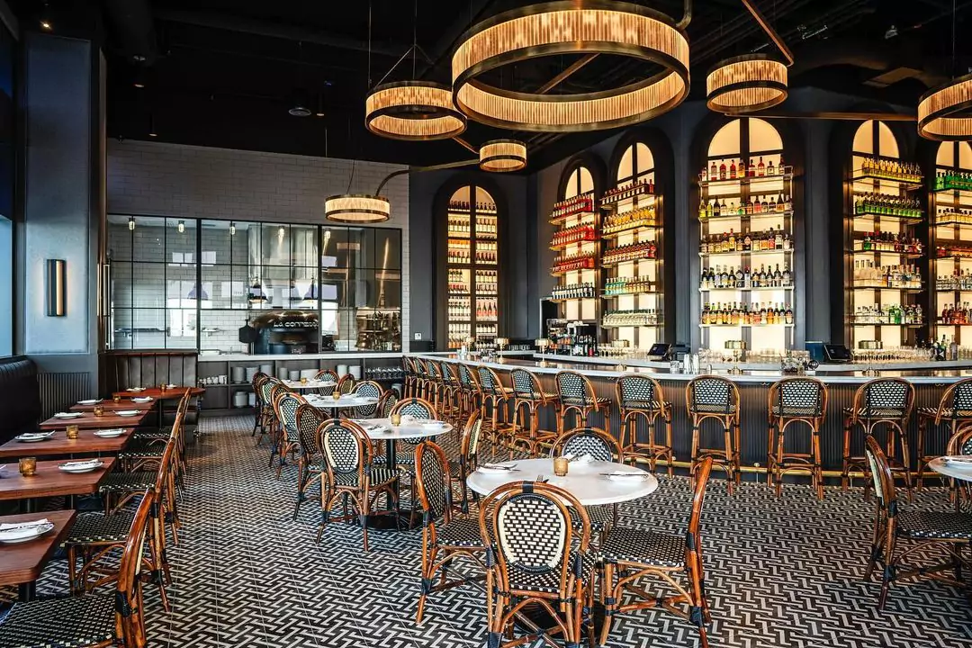 Swank interior at high-end Italian restaurant La Connessa, featuring white and black patterned tile floors, European style blue and white wicker chairs, contemporary circular lighting fixtures, a full wall bar with specialty liquor bottles, and white brick and rich blue painted walls