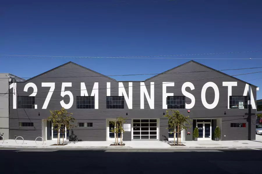 Outside street view of dark gray painted modern industrial building with 1275 Minnesota painted in large white block lettering on exterior
