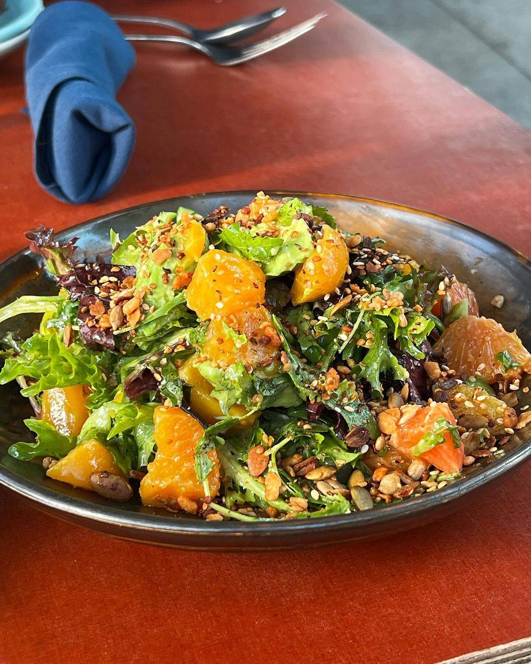 Close up photo of salad with baby spring greens, citrus, golden beets, and sunflower seed granola from Firefly San Francisco