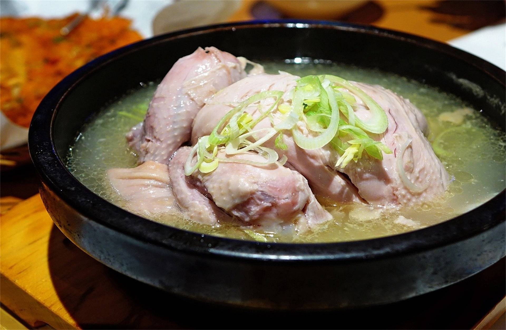 Close up view of dish with whole chicken in broth with green onion garnish at Hulu Wa China Bistro in SF