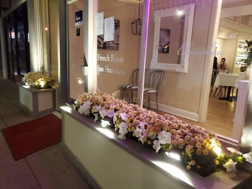 Exterior Sidewalk view at night of Chou Chou restaurant with flower boxes in the window and diners sitting at a white tablecloth lined table