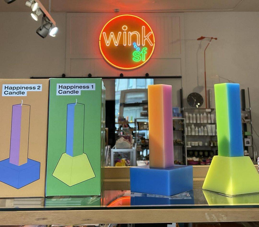 Photo of Multi colored “Happiness” candles with Wink SF Neon Sign in the background