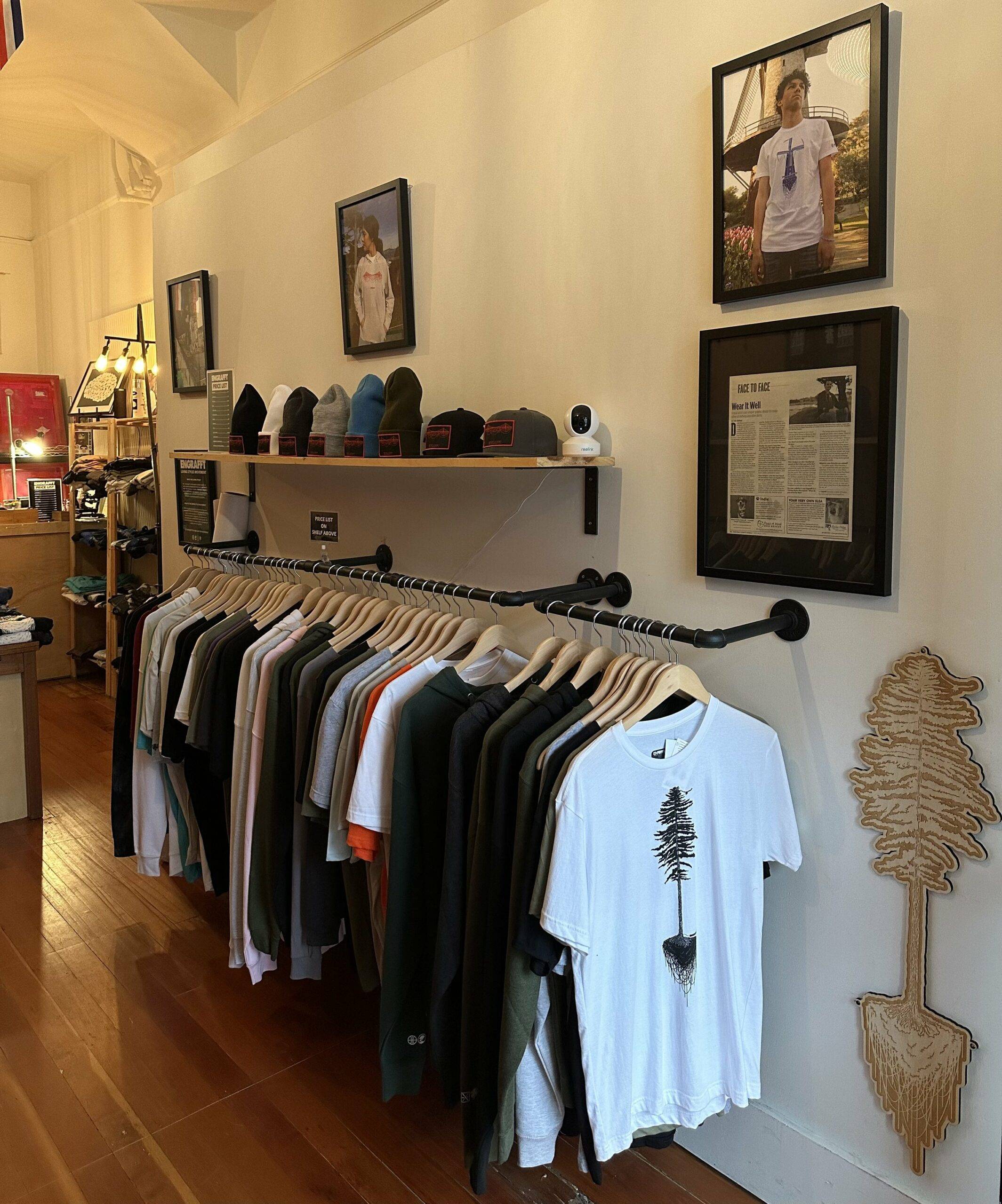 Interior View of Engrafft in SF’s Richmond District with graphic tees hanging on rack, beanies on shelf, and other clothing items in the background