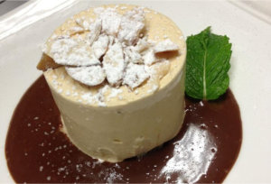 Specialty dessert custard cake with chocolate sauce and topped with almonds and powdered sugar from L’Ardoise Bistro