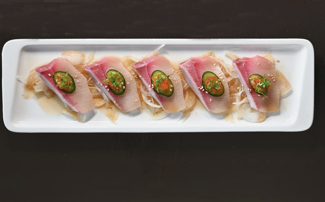 Plate of Fresh Crudo topped with Sliced Jalapenos and Sesame Seeds, laid on top of sliced pickled onions