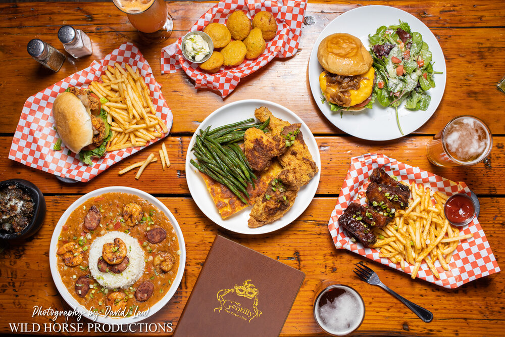 Wood Table topped with a number of classic Southern and Creole dishes & a menu book that says Gentilly on the front