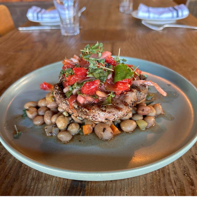 Grilled pork chop topped with heirloom tomato and microgreen slaw atop a bean ragu