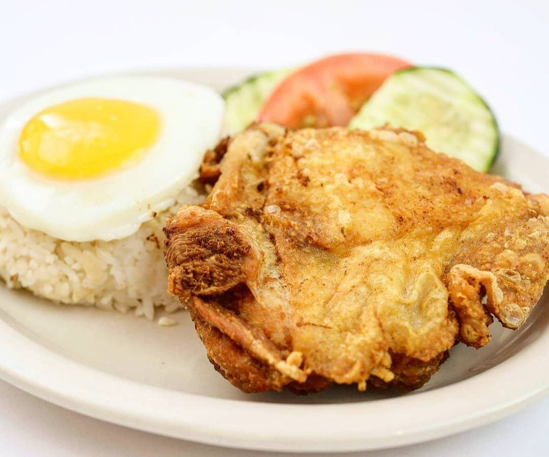 Plate of fried chicken, white rice topped with a fried egg, and sliced cucumbers and tomatoes at Tselogs