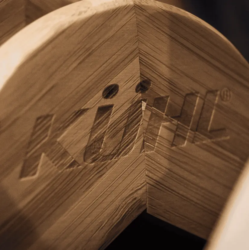 Close up image of light wood curved block that has “Kuhl” etched in to the wood