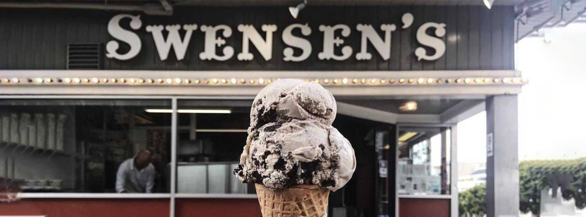 Ice Cream cone with a double scoop of cookies and cream ice cream and the original SWENSEN’S storefront in the background