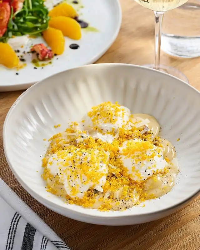 White bowl filled with ravioli topped with over easy eggs, bread crumbs, and shredded parmesan cheese