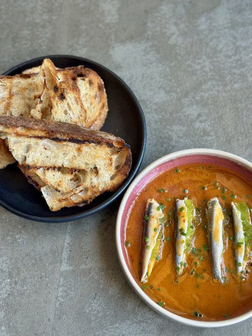 Dish of 4 anchovies in a red pasta sauce topped with capers and a green oil-based sauce, with a side of two pieces of grilled and sliced ciabatta