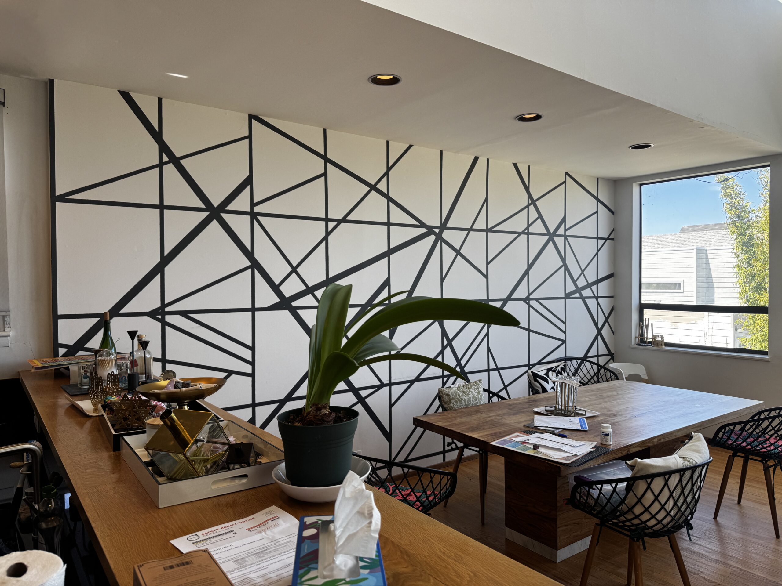 Dining area before prep, seen from the stair landing, with a black geometric line pattern on the back wall, oak cabinets on the left, windows on the right, and a dog in the foreground