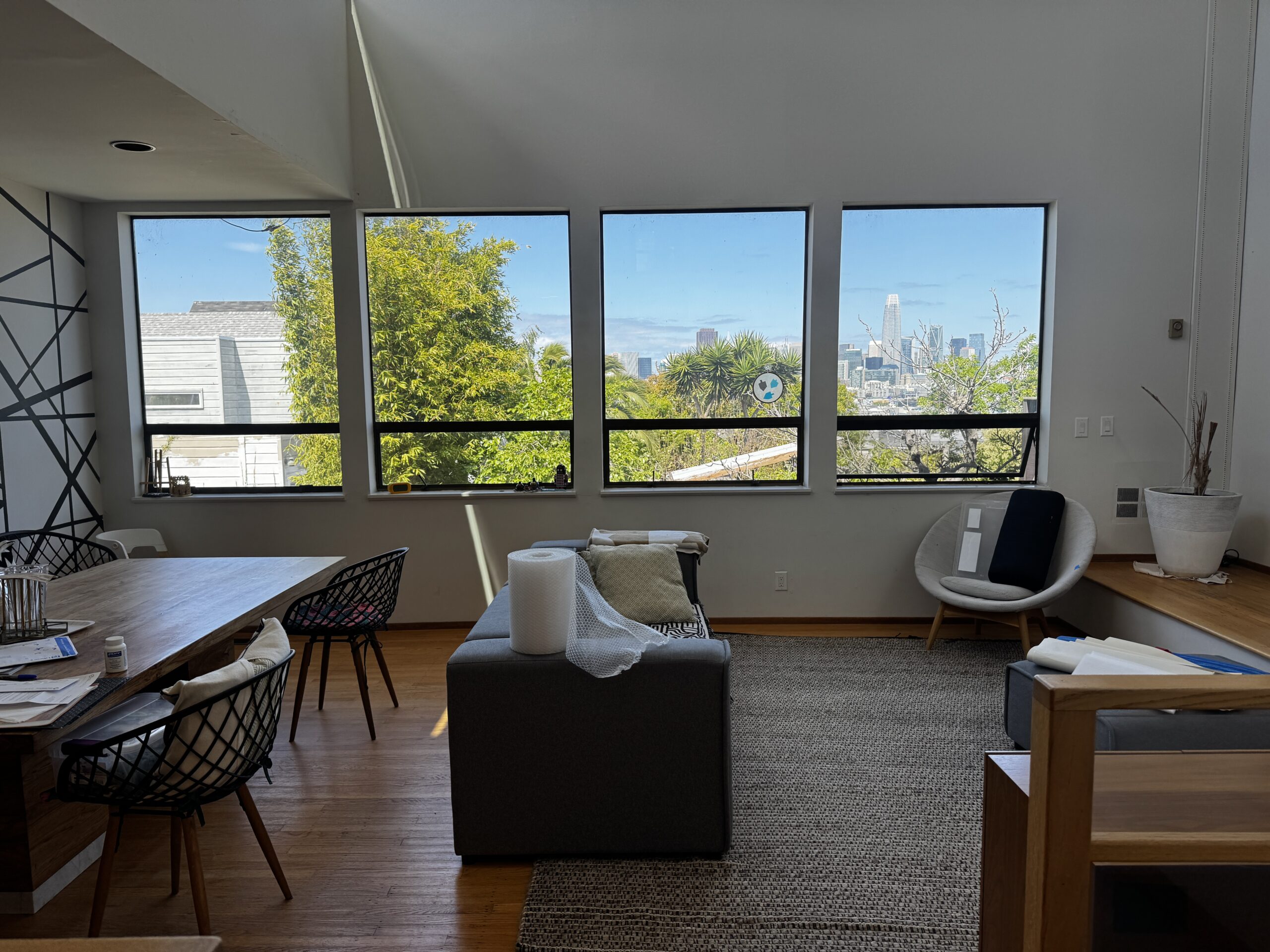 Living room before prep, with a dark gray sofa, a dining table with black wire chairs, and a black striped accent wall, facing four windows with a view of the downtown skyline